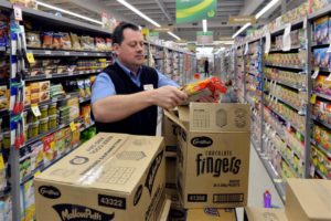 A grocer unpack product from a cardboard box. 